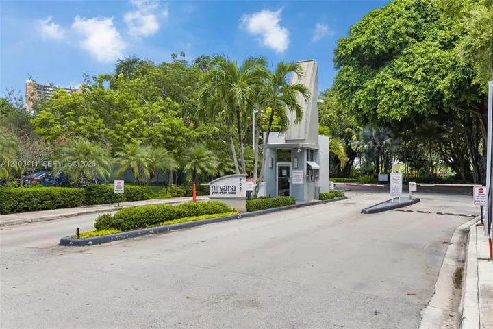 Gated entry featuring a controlled-access security booth, paved roadway, and mature landscaping