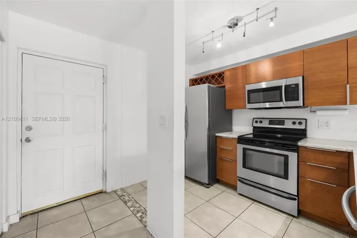 Kitchen featuring horizontal-grain wood cabinetry, integrated wine storage, stainless steel appliances, light-toned stone-finish countertops, and multi-directional track lighting