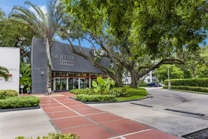 Modern exterior facade featuring dark-toned concrete cladding, full-height glass storefront windows, a paved pedestrian walkway, and mature oak landscaping