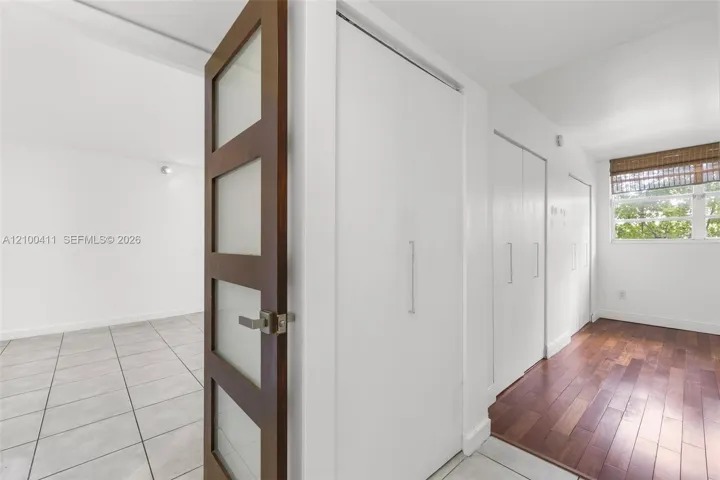 Wood-finish flooring, white built-in floor-to-ceiling closets with chrome hardware, and a dark wood door featuring four frosted glass panels