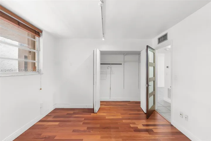 Wood-finish flooring, multi-pane window with wood-trim surround, bi-fold closet doors with integrated shelving, and a glass-paneled interior door