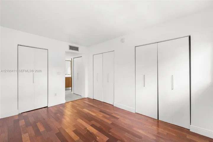 Wood-finish flooring and multiple built-in floor-to-ceiling closets with white panel doors and vertical silver pulls