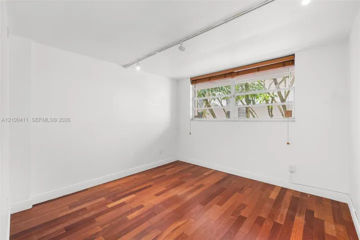Interior room featuring wood-finish flooring, ceiling-mounted track lighting, and a horizontal window with slatted wood-tone blinds