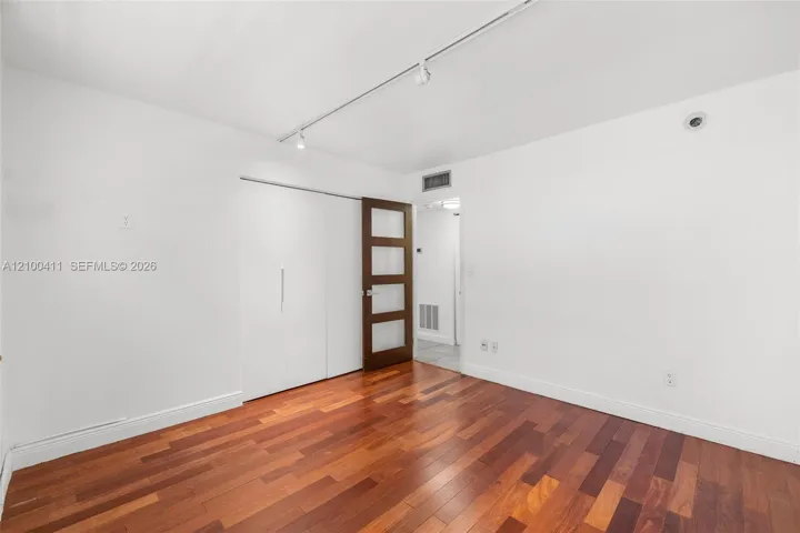 Room featuring wood-finish flooring, white walls, track lighting, built-in sliding closet doors, and a four-panel glass-inset door