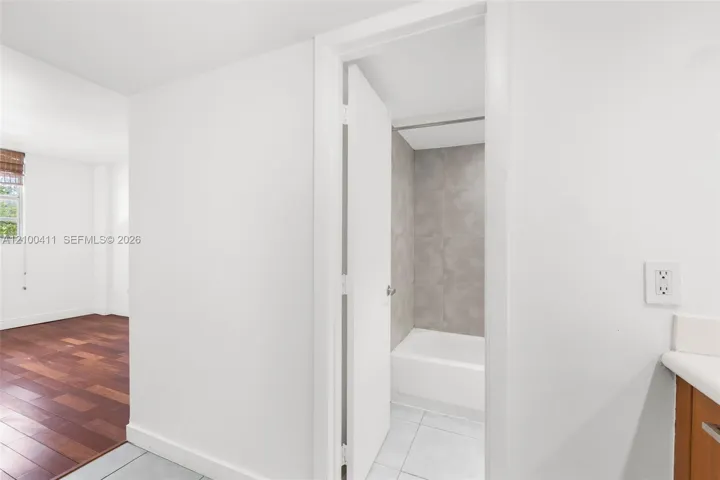 Wood-finish flooring, white walls, and a bathroom featuring a white porcelain tub with grey wall tiling