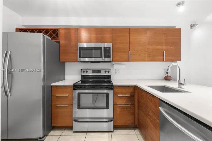 Kitchen featuring wood-finish cabinetry, built-in wine storage, stone-finish countertops, stainless steel appliances, and a stainless steel undermount sink with a gooseneck faucet
