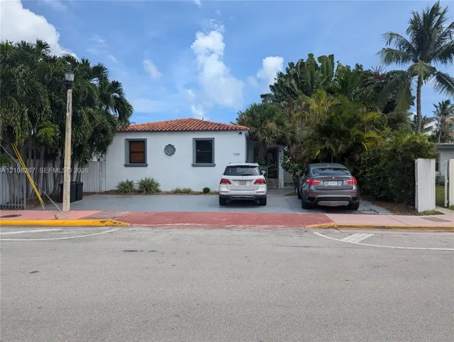 Stucco exterior featuring a terracotta tile roof, paved driveway, and mature landscaping