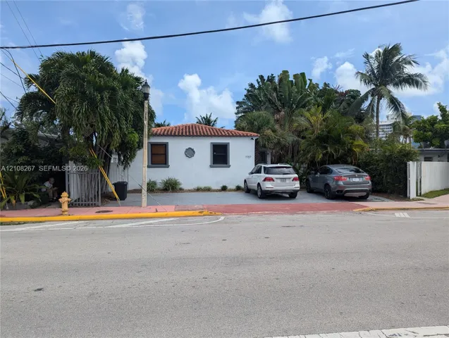 Stucco exterior featuring a terracotta-tiled hip roof, multi-car paved parking area, and mature tropical landscaping