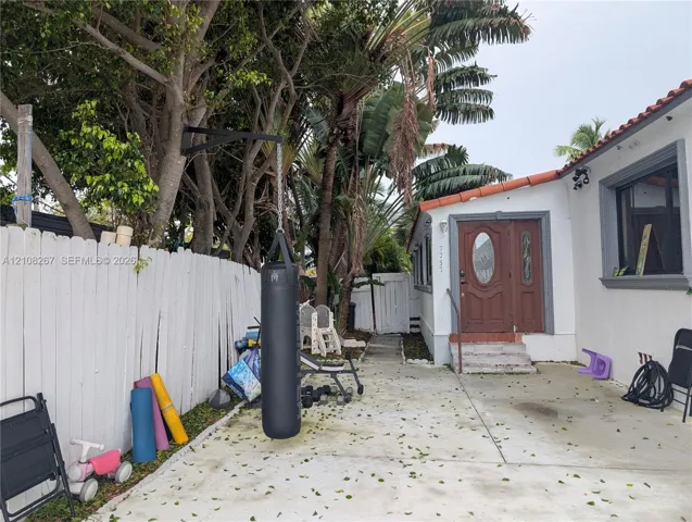 Exterior space featuring concrete hardscaping, a white wood fence, and a stucco-finish residence with a terracotta-tile roof accent and a wood-paneled arched entry door