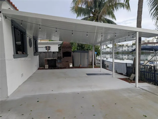Covered patio featuring a concrete slab, built-in brick fireplace, and metal roof structure overlooking a canal