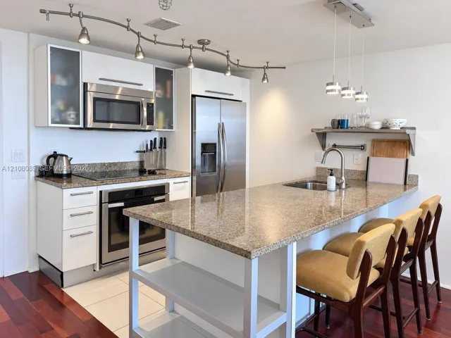 Kitchen featuring stone countertops, stainless steel appliances, white cabinetry with glass-front uppers, an integrated island with shelving, and track lighting
