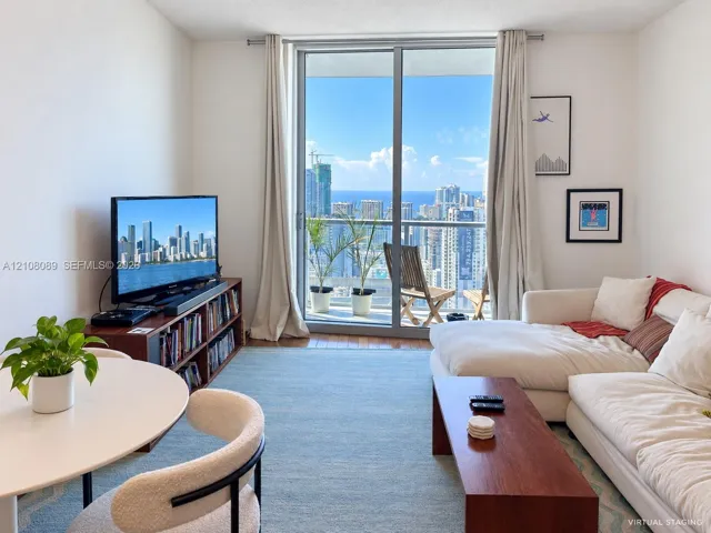 Living area featuring floor-to-ceiling glass sliding doors, balcony access, and expansive urban and water scenery