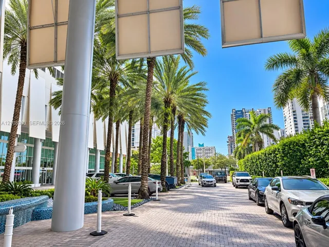 Paver-stone drive featuring towering palm trees, a blue mosaic tile water feature, structural columns, and large-scale architectural wall panels