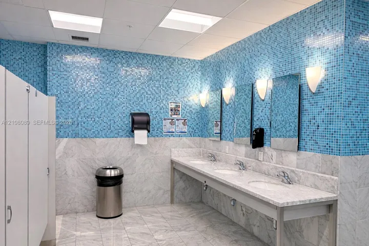 Multi-station stone vanity with integrated sinks, polished stone flooring, blue mosaic tile wall accents, and wall-mounted sconce lighting