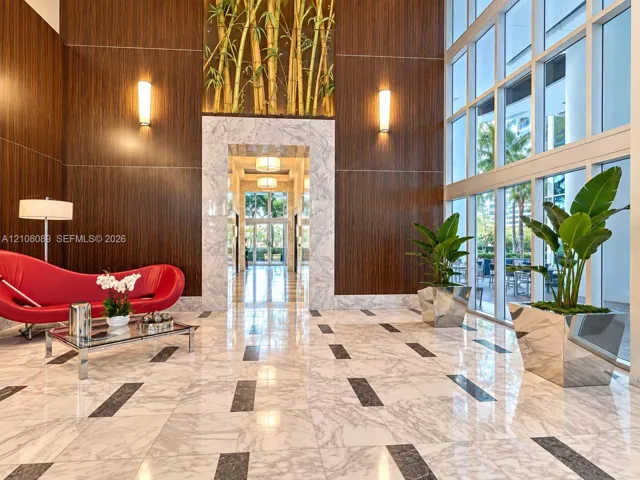 Lobby featuring floor-to-ceiling windows, polished stone flooring with decorative inlay, wood-paneled walls, stone-trimmed entryway, and integrated wall-mounted lighting