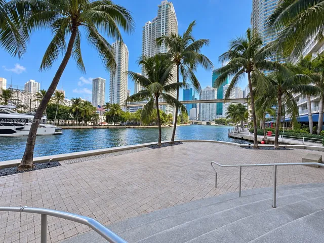 Waterfront paved terrace with stone-finish pavers, metal railings, and integrated palm tree landscaping