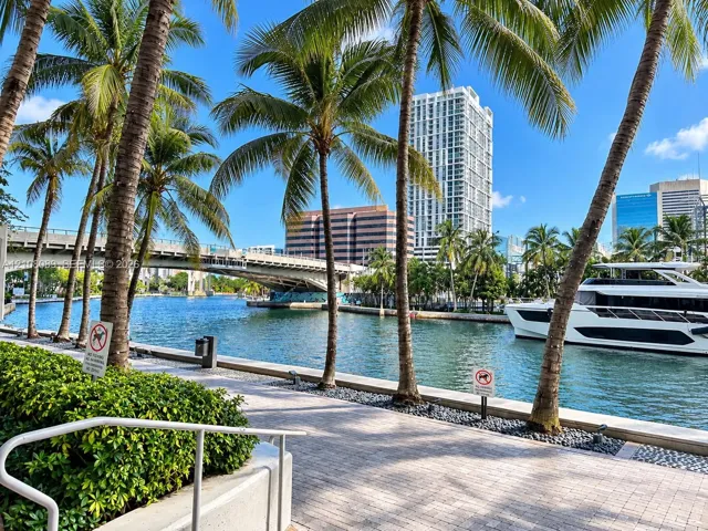 Waterfront promenade featuring stone paver walkways, mature palm trees, and bulkhead retaining walls along a waterway