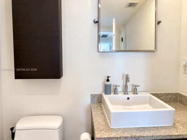 Bathroom vanity featuring a vessel sink, stone-finish countertop, wall-mounted dark wood-finish cabinetry, and a chrome-framed mirror with chrome widespread faucet