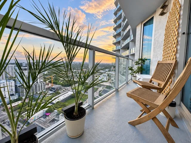 Covered balcony featuring glass railing, metal framework, and concrete flooring with sunset horizon backdrop