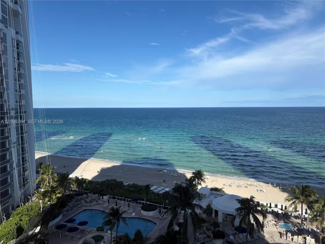 High-rise balcony exposure featuring direct ocean frontage, a multi-level swimming pool, spa, and tropical palm landscaping