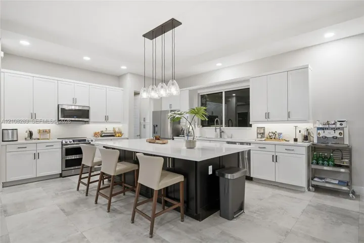 Kitchen featuring white Shaker-style cabinetry, a central island with a contrasting dark base and stone countertop, stainless steel appliances, recessed ceiling lighting, and tile flooring