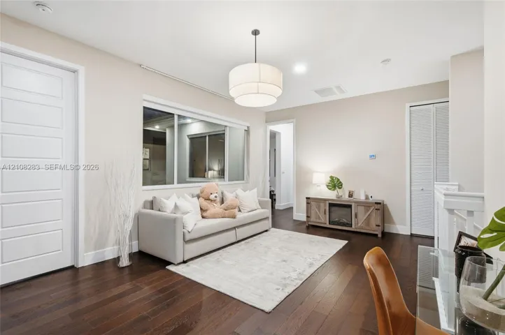 Dark wood-finish flooring, multi-panel interior door, tiered drum pendant lighting, large sliding window, and louvered closet doors