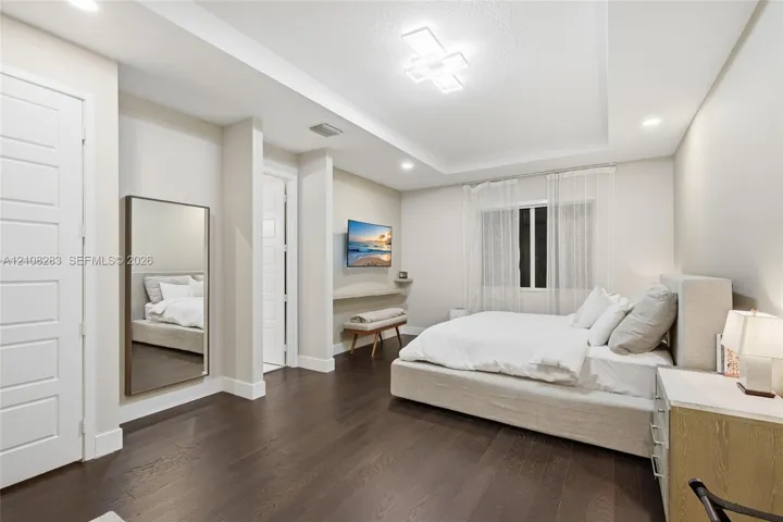 Bedroom featuring wood-finish flooring, tray ceiling with recessed and geometric modern lighting, and a wall-mounted floating display ledge