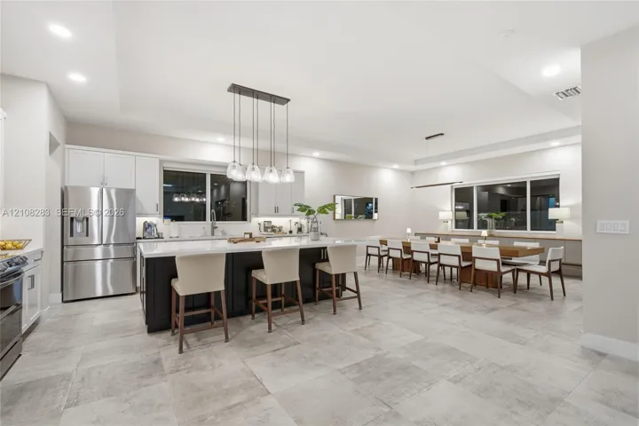 Kitchen featuring a center island with contrasting cabinetry, stone-finish countertops, stainless steel appliances, recessed ceiling lighting, and large-format tile flooring