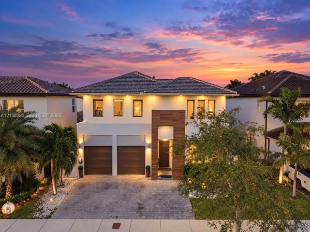 Two-story residence featuring a paved driveway, dual-car garage with wood-finish doors, contemporary tile roof, and textured stone facade accents