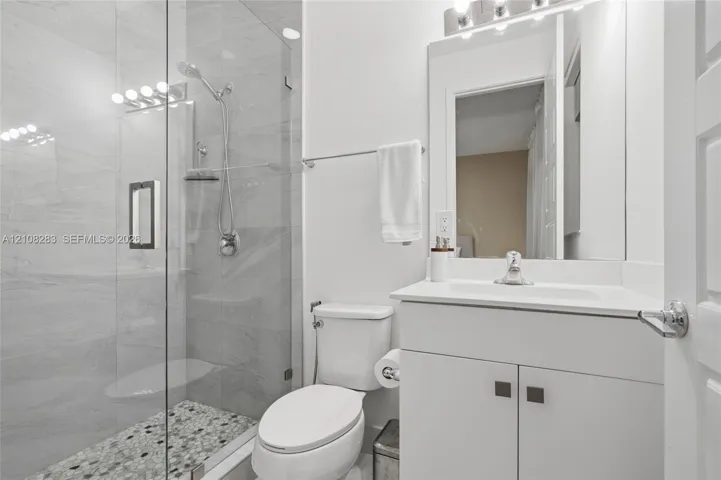 Glass-enclosed shower with stone-tile flooring, wall-mounted handheld shower head, vanity with integrated basin, and modern light fixture