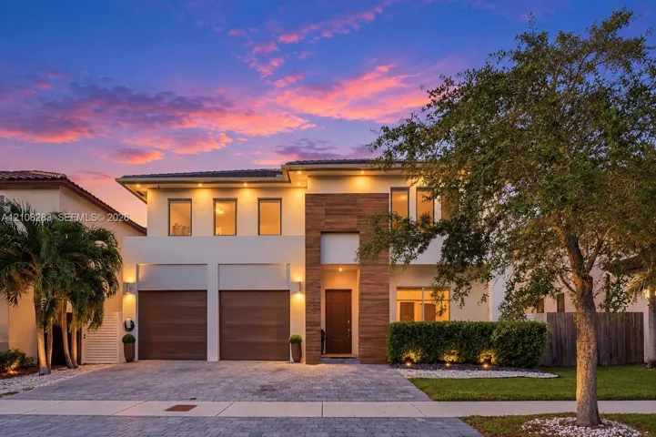 Two-story contemporary exterior featuring a light-toned stucco facade, wood-finish accents, integrated soffit lighting, a two-car garage, and a paver driveway