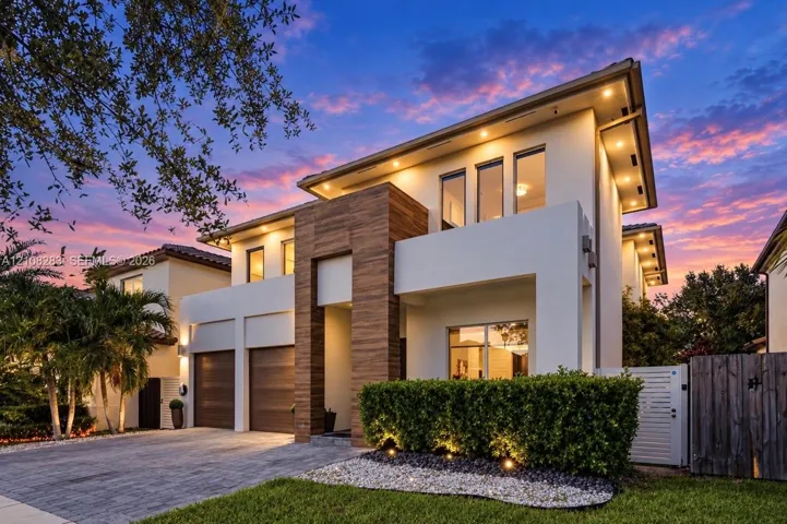 Contemporary exterior featuring smooth stucco finish, vertical wood-paneling accents, recessed soffit lighting, two-car garage with wood-finish doors, and paved driveway