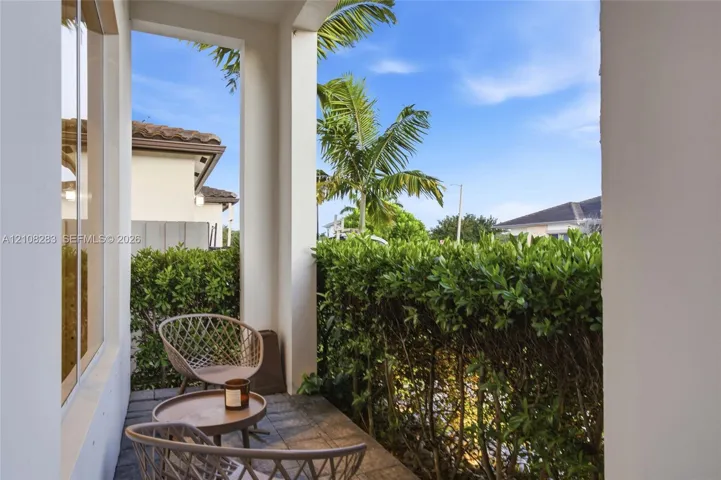 Covered patio featuring stone-tile flooring, structural support columns, and dense, manicured privacy hedging