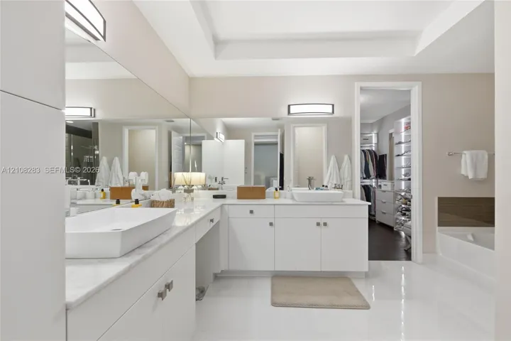 Dual vanity featuring rectangular vessel sinks, white stone countertops, white cabinetry with brushed metallic hardware, and full-width wall mirrors