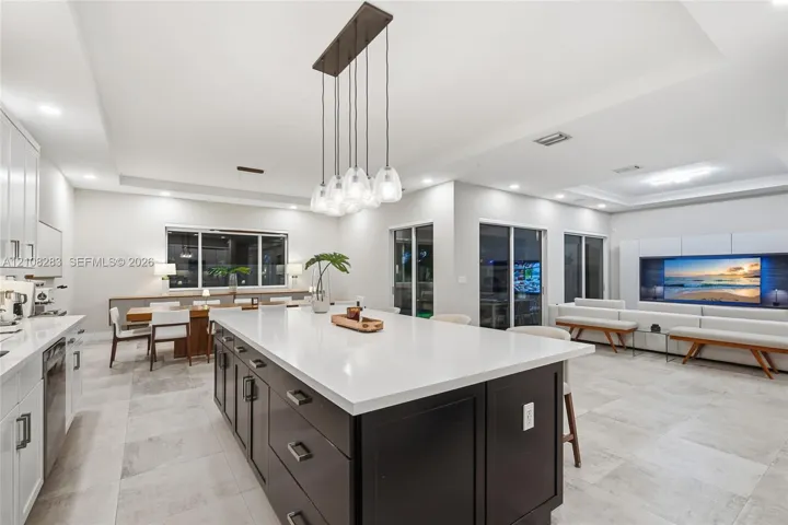 Kitchen featuring a center island with contrasting cabinetry, stone-finish countertops, tile flooring, built-in media console, and multi-pendant lighting