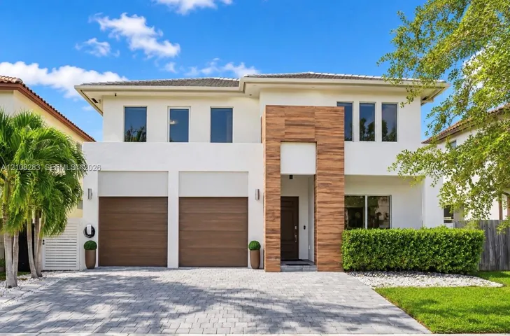 Two-story exterior featuring smooth stucco finish, vertical wood-plank architectural cladding, paver driveway, and dual wood-finish garage doors