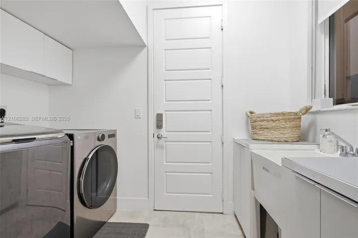 Laundry area featuring white cabinetry, a utility sink with a faucet, five-panel door, and tiled flooring
