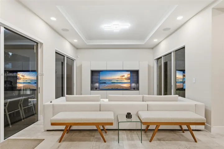 Living space featuring a tray ceiling, recessed lighting, large-format tile flooring, built-in media cabinetry, and multiple sliding glass doors