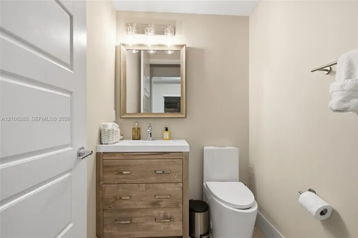Bathroom featuring a wood-finish vanity with a rectangular sink, wall-mounted light fixture, framed mirror, and elongated dual-flush toilet