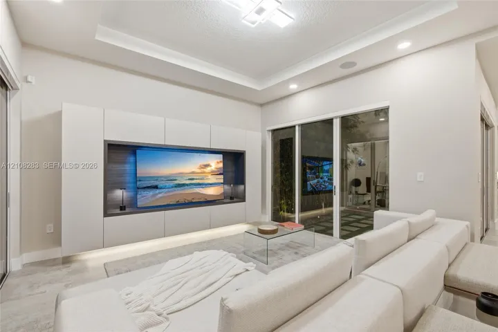 Living area featuring a tray ceiling with recessed lighting, custom floor-to-ceiling built-in media cabinetry with integrated lower illumination, and glass sliding doors