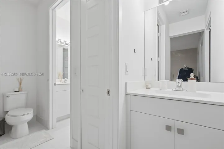 Bathroom featuring a white vanity cabinet with a stone-top integrated sink, a full-height wall mirror, a polished chrome faucet, and a standard-height toilet