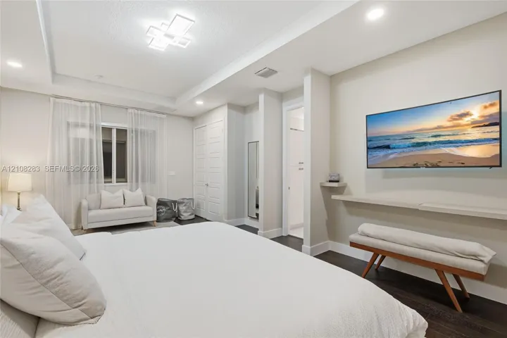 Tray ceiling with geometric flush-mount lighting, dark wood-finish flooring, recessed lighting, and a wall-mounted floating shelf