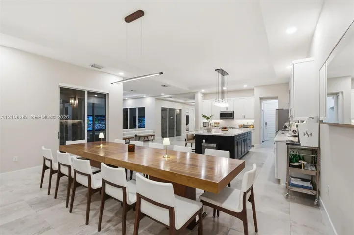 Open concept kitchen and dining area featuring large format tile flooring, a central kitchen island with contrasting cabinetry, white shaker-style wall cabinets, and recessed lighting