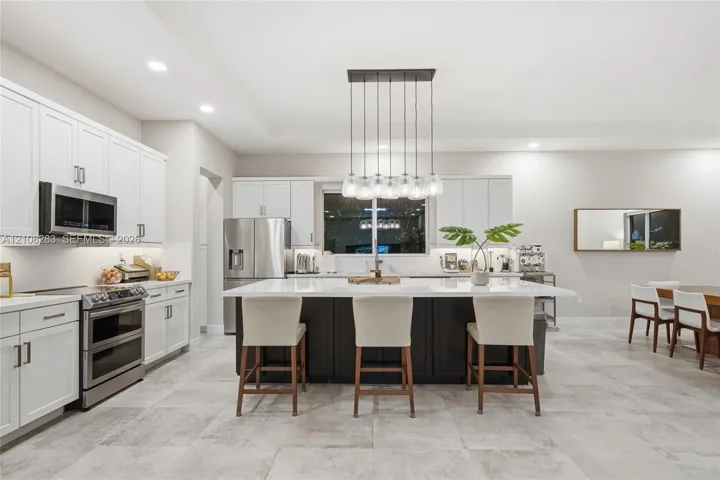 Kitchen featuring white shaker-style cabinetry, a contrasting dark-toned kitchen island with a light-toned solid surface countertop, stainless steel appliances, and tile flooring