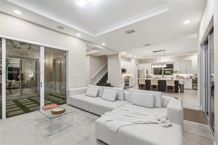 Open-concept living space featuring a tray ceiling, recessed lighting, large sliding glass doors, neutral tile flooring, and a kitchen with an oversized island and white cabinetry