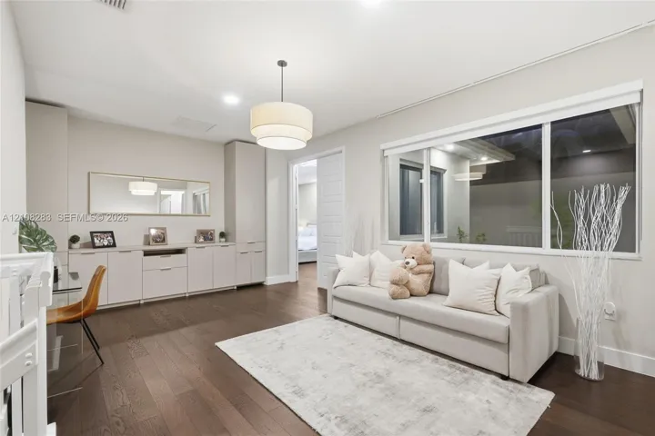 Spacious room featuring wood-finish flooring, extensive built-in cabinetry, a modern tiered drum pendant light, and a large horizontal window
