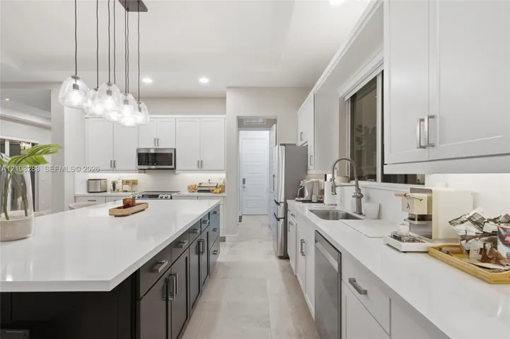 Kitchen featuring a central island with a solid-surface countertop, white shaker-style cabinetry, stainless steel appliances, and multi-light pendant fixture