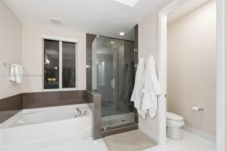 Built-in soaking tub with a tiled surround, glass-enclosed shower, polished finish flooring, and wall-mounted metal fixtures