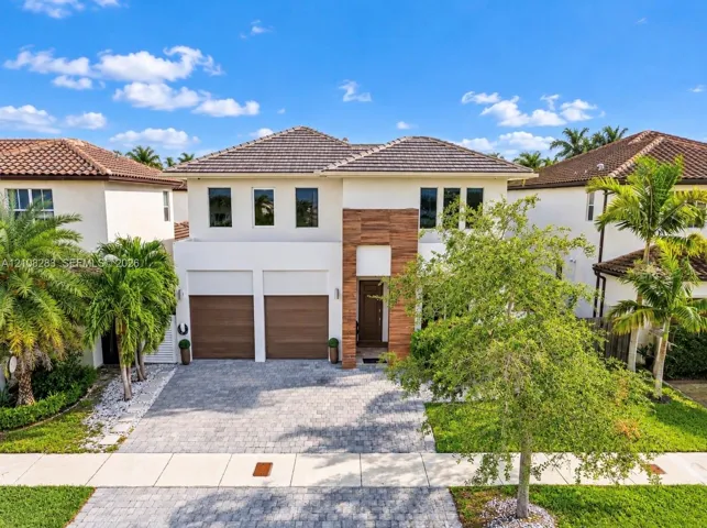 Two-story exterior featuring a stucco facade, wood-slat vertical accents, a concrete tile roof, dual garage doors, and a paver driveway