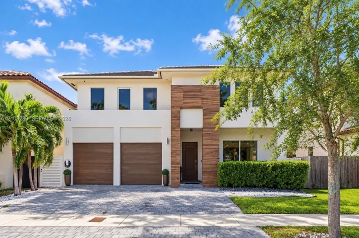 Two-story exterior featuring light-toned stucco, wood-finish accents, a paver driveway, and an attached two-car garage
